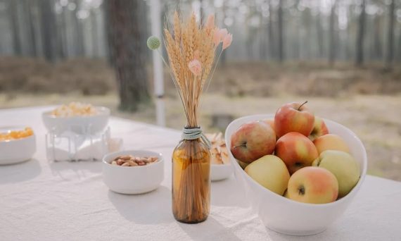 Rustic outdoor table setup featuring apples, nuts, and dried flowers in a vase, creating a cozy autumn vibe.