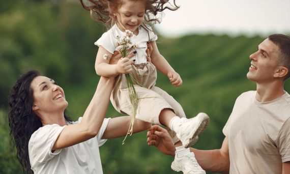 Happy family enjoying playful outdoor moment, lifting child in summer day.