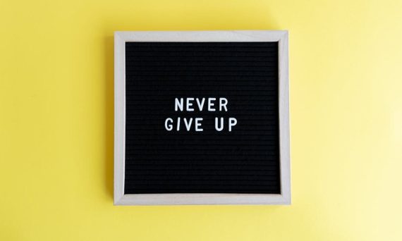 Black felt board with 'Never Give Up' on a bright yellow background for motivation.